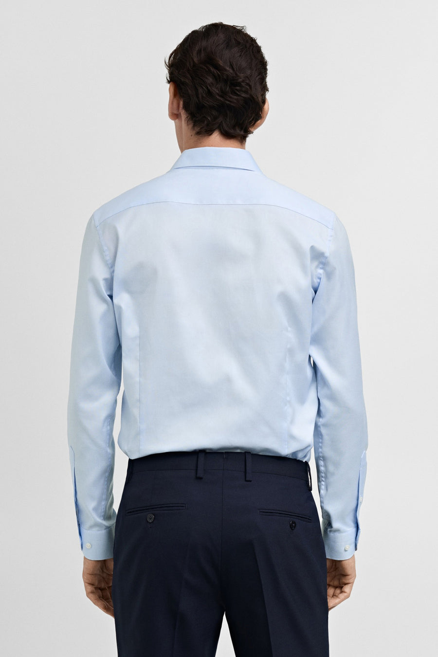 Chemise bleu clair à manches longues de MANGO, vue de dos, portée sur un pantalon bleu foncé.