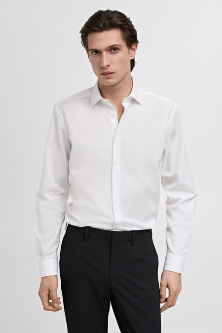 Blouse blanche à manches longues de MANGO, associée à un pantalon noir sur un fond blanc uni.