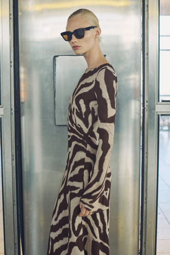 Robe brune à longues manches de MANGO, avec un imprimé zèbre et portée avec un chapeau de soleil.