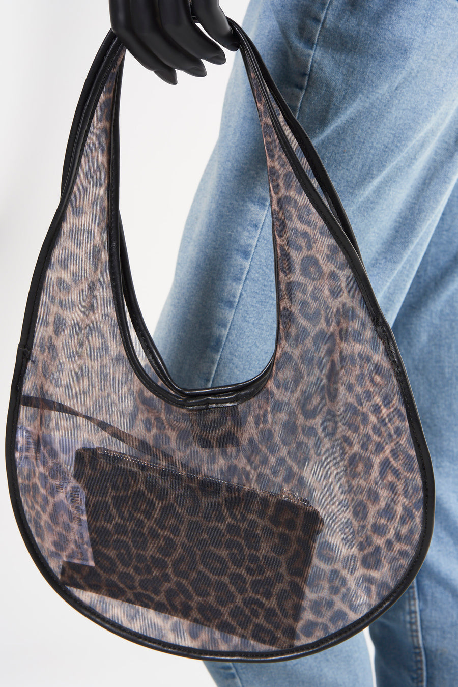 Doorzichtige handtas met luipaardprint, zwarte details, gedragen door een mannequin met denim broek.