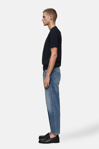 Jean tapered MANGO en denim bleu medium, avec une coupe décontractée et des loafers noirs.