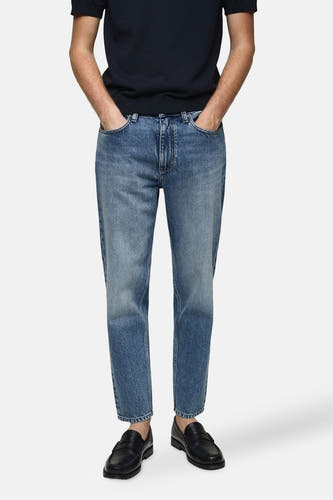 Jean tapered bleu de MANGO, associé à des loafers noirs et un T-shirt bleu marine.