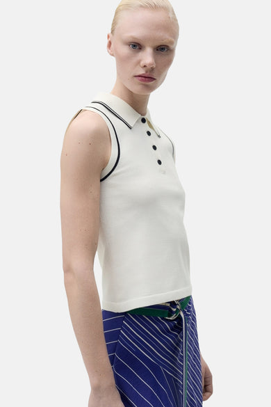 Polo blanc de MANGO, sans manches avec une patte noire, porté avec une jupe rayée bleue.