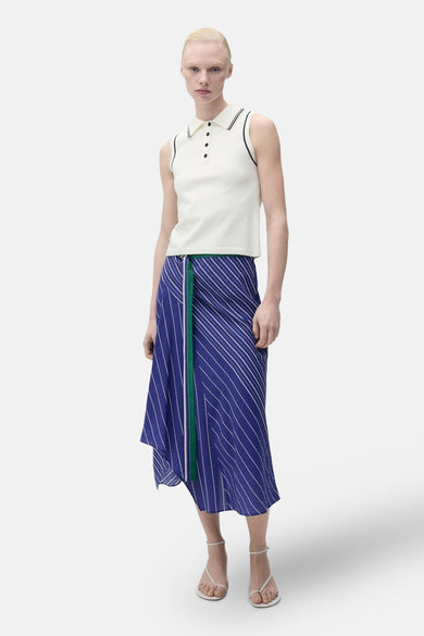 Polo blanc de MANGO avec des détails noirs sur la en et les manches, porté avec une jupe rayée bleue.