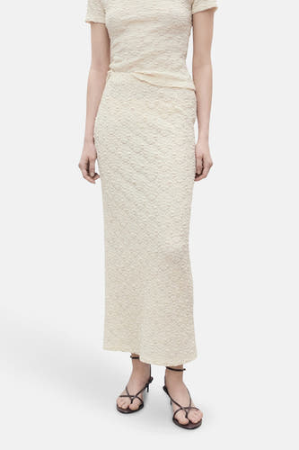 Longue jupe écru de MANGO, avec un motif de fleurs texturé et associée à des sandales noires.