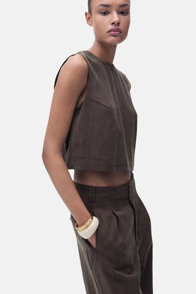 Blouse brune sans manches de MANGO, associée à un pantalon de la même couleur et une unche blanche.