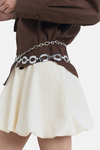 Robe courte couleur écru de MANGO, avec un bord froncé et une ceinture en chaîne argentée à la taille.
