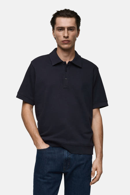 Donkerblauwe polo sweater van MANGO, gedragen met een donkere jeans en één hand in de zak.
