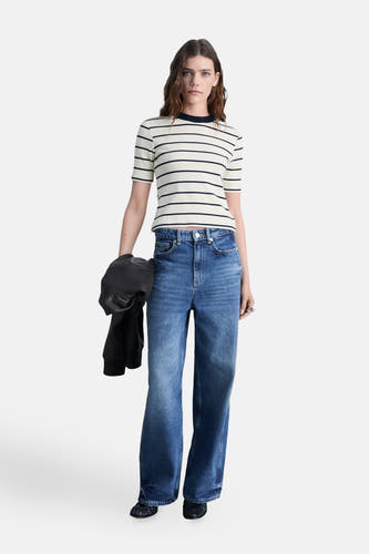 T-shirt rayé blanc à manches courtes de MANGO, associé à des jeans larges et une veste en cuir noire.