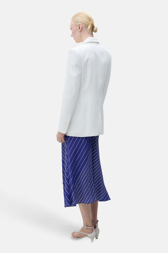 Longue jupe bleue à rayures de MANGO, portée avec un blazer blanc et des sandales à talons.