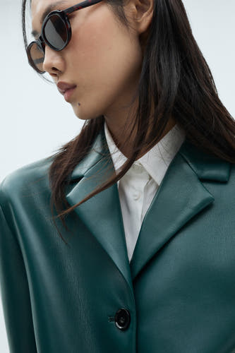 Blazer courte bleue de MANGO, portée sur une chemise blanche et associée à des lunettes de soleil rondes.