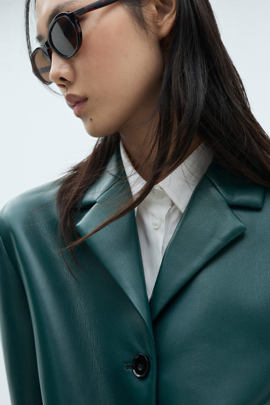 Blazer courte bleue de MANGO, portée sur une chemise blanche et associée à des lunettes de soleil rondes.