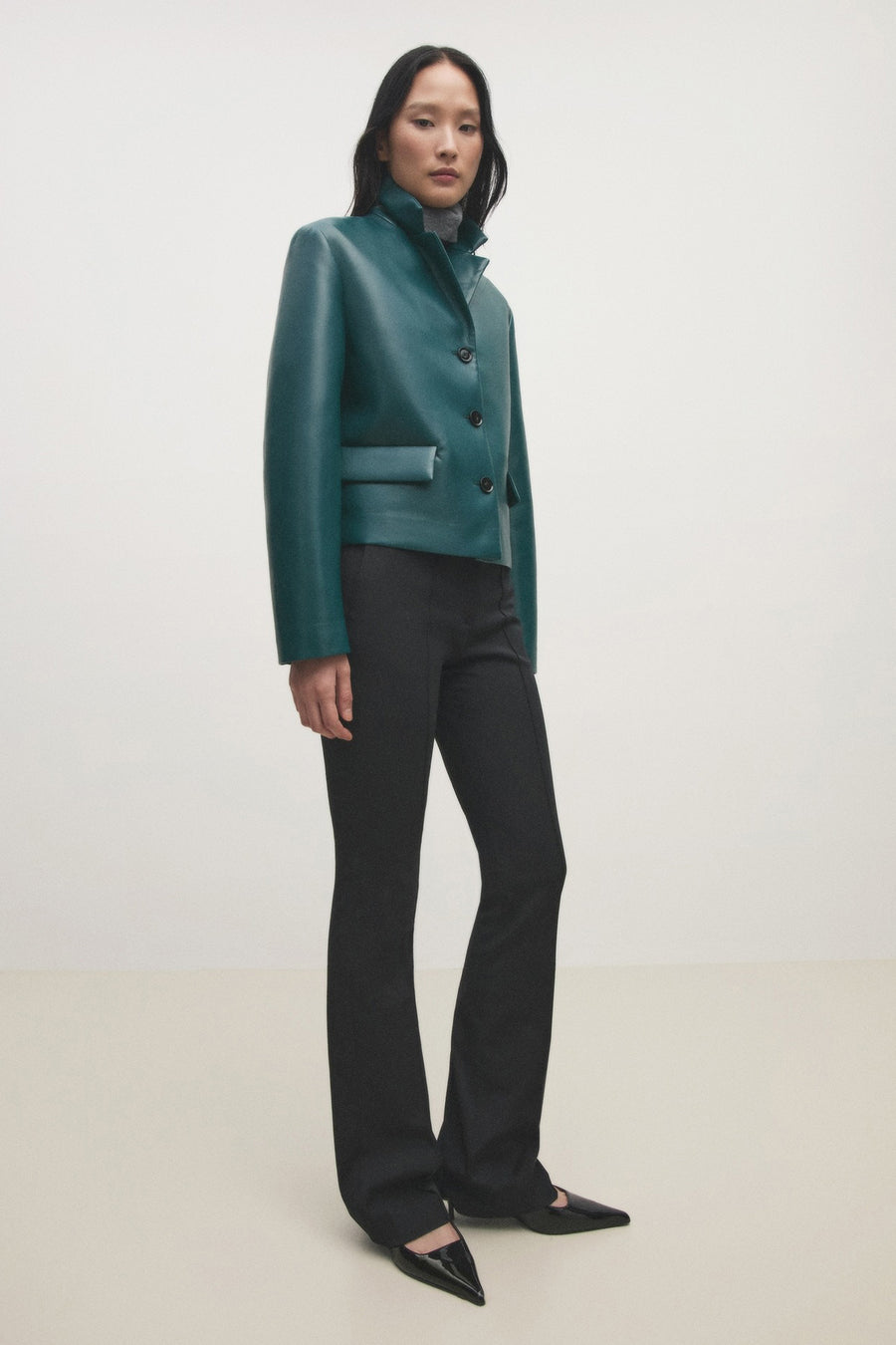 Blazer courte bleue de MANGO, à manches longues et fermeture à boutons, portée avec un pull à col roulé gris et un pantalon noir.