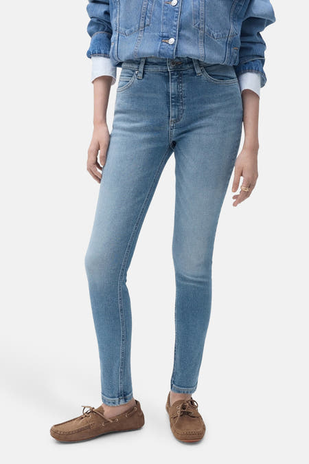 Jean skinny en denim bleu clair de MANGO, complété par une veste en denim et des mocassins marrons, vue latérale.