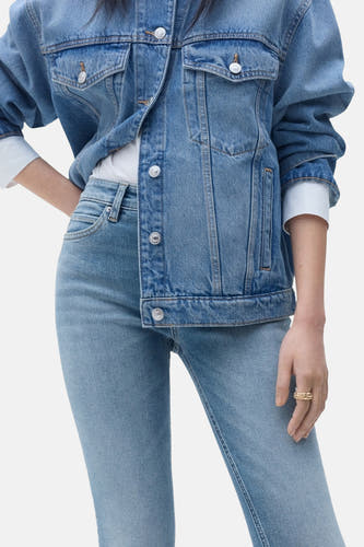 Jean skinny bleu clair de MANGO, associé à une veste en denim et des bagues d'or.