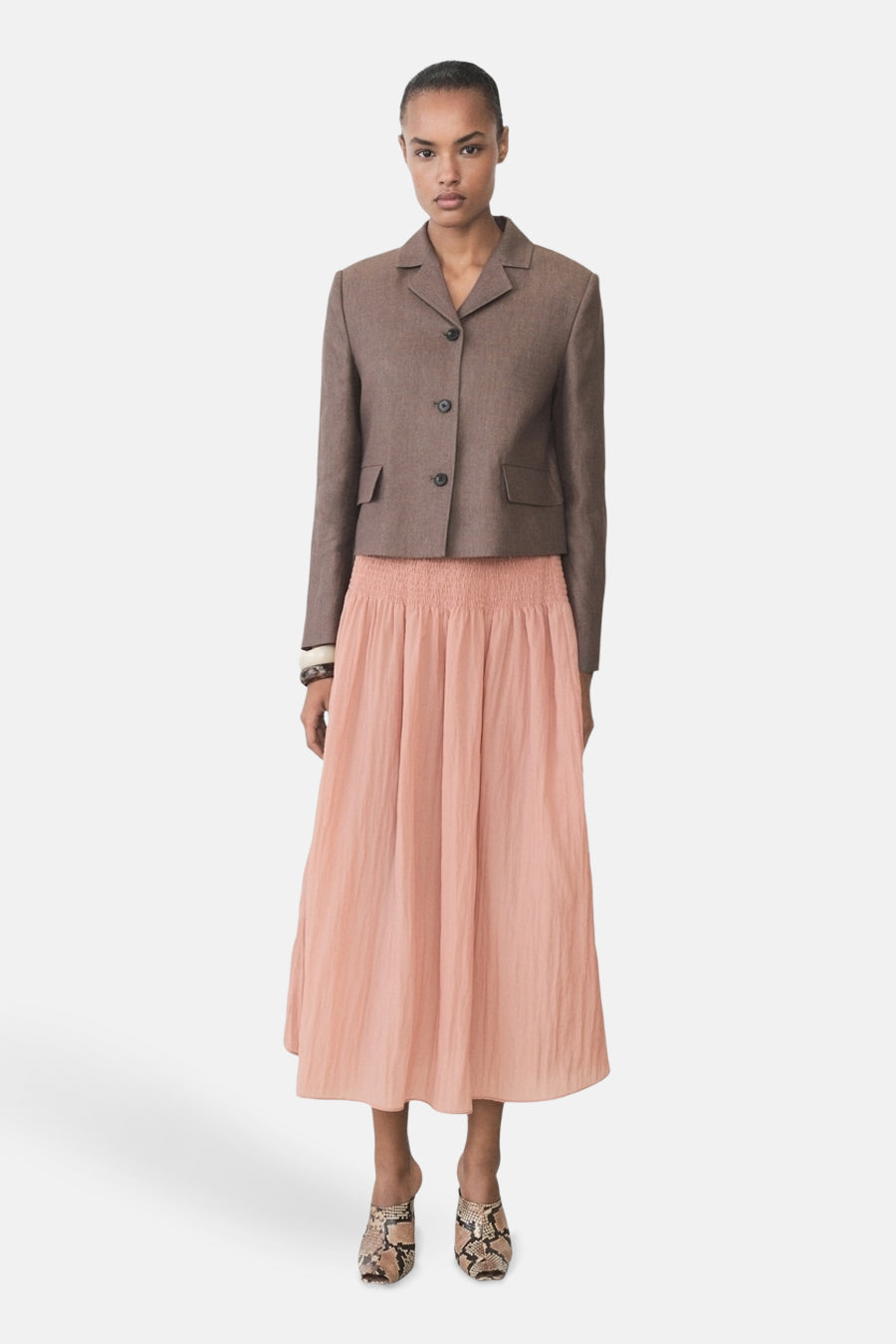 Vrouw in bruine blazer, roze rok, en slangenprint muiltjes.