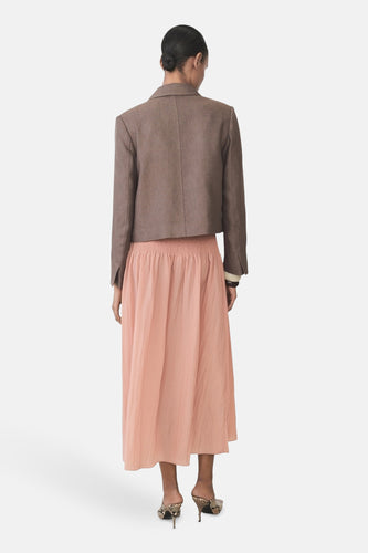 Vrouw van achteren, bruine blazer, perzikkleurige rok, slangenleren hakken.
