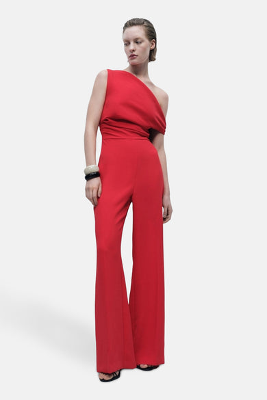 Combinaison rouge de MANGO, avec une ligne d'épaule asymétrique et des manches larges, stylisée avec des bracelets.