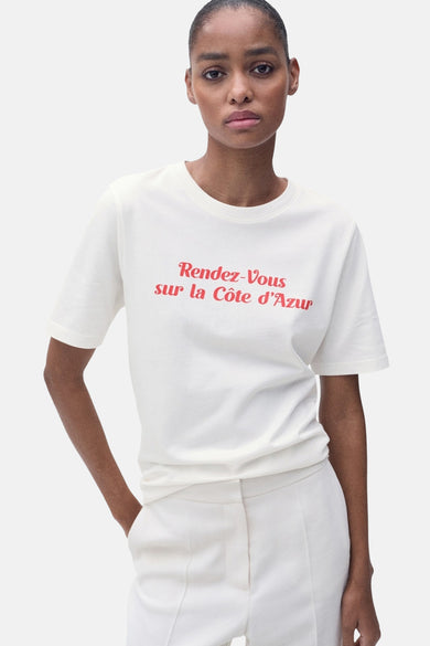 T-shirt blanc à manches courtes de MANGO, dos, avec un pantalon léger assorti et des chaussures marrons.
