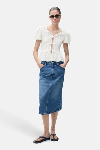 Blouse blanche à manches courtes de MANGO, avec un détail ouvert et portée avec une jupe en denim.