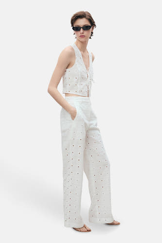 Blouse blanche sans manches de MANGO, avec des détails brodés, portée avec un pantalon coordonné et un chapeau.