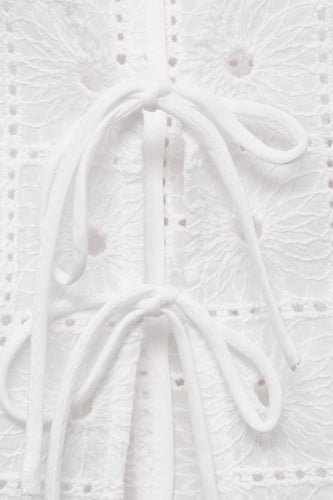 Wit kledingstuk met broderie en knoopdetails.
