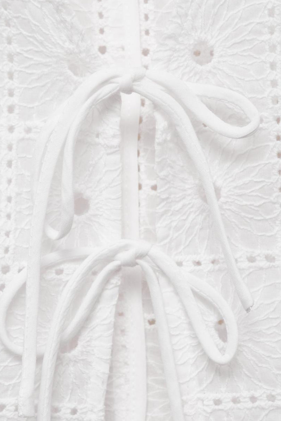 Wit kledingstuk met broderie en knoopdetails.
