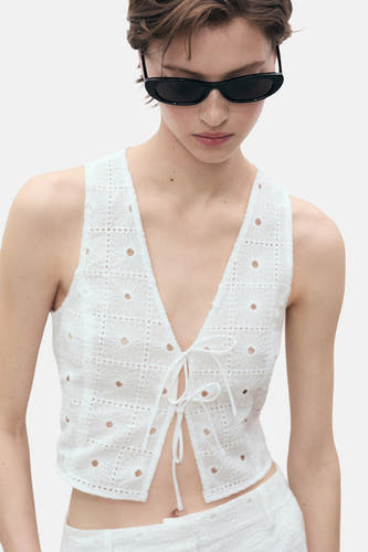 Blouse sans manches blanche de MANGO, avec des détails en dentelle et une fermeture éclair à l'avant.