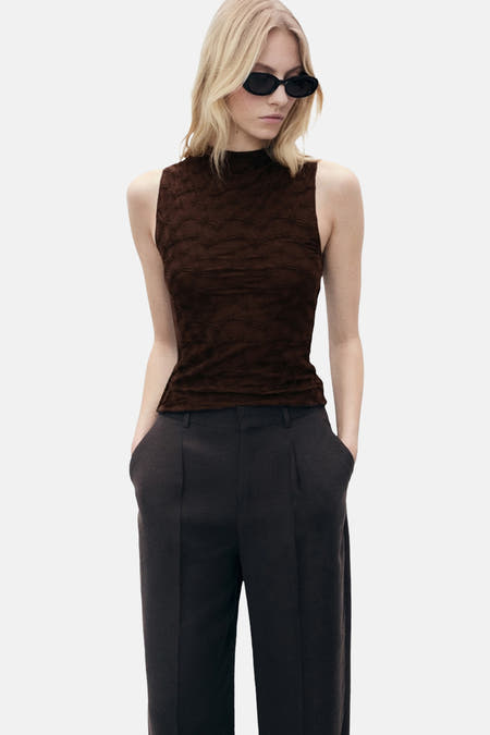 Blouse sans manches marron de MANGO, avec une texture pliée et associée à un pantalon foncé.