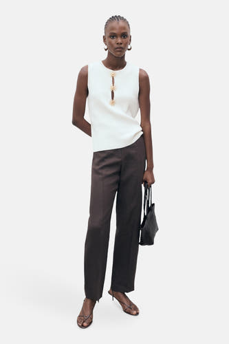 Chemisier blanc sans manches de MANGO, avec boutons décoratifs dorés sur le devant, combiné avec un pantalon foncé et des sandales.