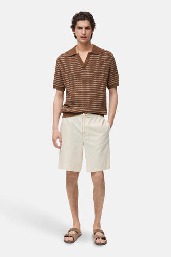 Crème court de MANGO, avec une ceinture élastique et un cordon de serrage, associé à une polo rayée marron et des sandales.