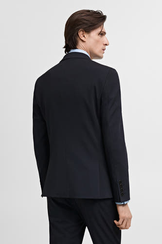 Blazer bleu de MANGO, vue de dos, portée sur une chemise bleu clair et un pantalon bleu foncé.