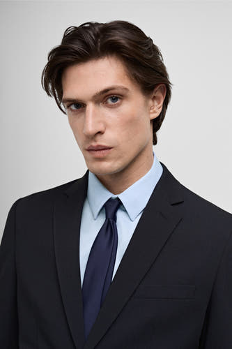 Blazer bleue de MANGO, portée avec une chemise bleu clair et une cravate bleu foncé.
