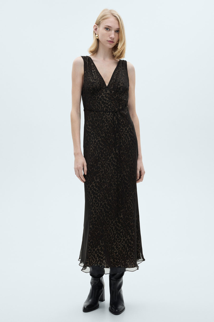 Zwarte mouwloze jurk van MANGO, met luipaardprint en een wikkeldesign, gecombineerd met zwarte leren laarzen.
