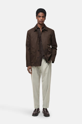 Pantalon gris MANGO, porté avec une chemise marron et un manteau, et des loafers marrons foncés.
