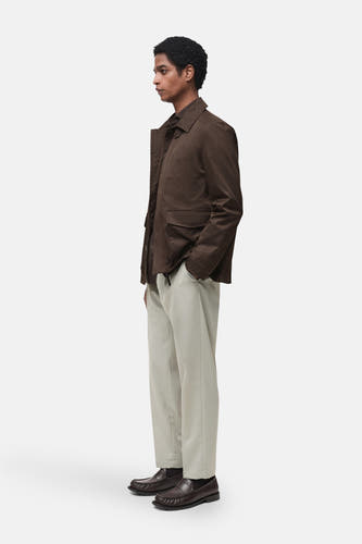 Pantalon gris MANGO, porté avec un manteau brun et des chaussures en cuir foncé, en vue de côté.
