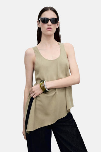 Blouse sans manches k kaki, de MANGO, avec une ligne de coupe asymétrique, portée avec un jean et un chapeau de soleil.