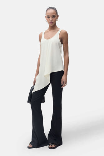 Blouse écru sans manches de MANGO, avec un design asymétrique et portée avec une jupe noire à longues et des sandales.