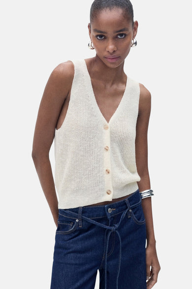 T-shirt écru de MANGO, avec col V et fermeture à boutons, associé à un jeans foncé et un bracelet en argent.