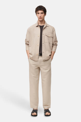 Manteau court écru de MANGO porté sur un T-shirt noir avec des pantalons beige coordonnés et des sandales noires.