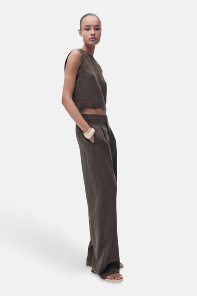 Pantalon marron de MANGO, avec des jambes larges et une pliure, porté avec un haut coordonné et un bracelet.