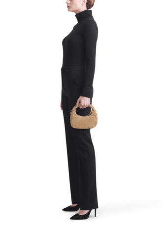 Sac à main beige Access® avec clous dorés et poignée courte, tenu par un mannequin.