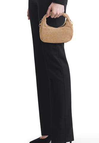 Sac à main beige en suède d'Access® avec clous dorés, tenu par une personne vêtue de noir.