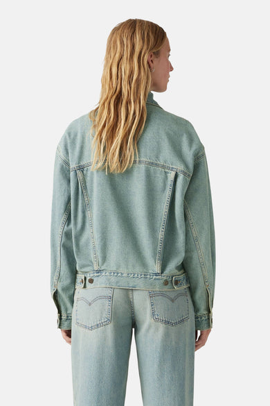 Vrouw met blonde haren van achteren in een denim jas en broek.

