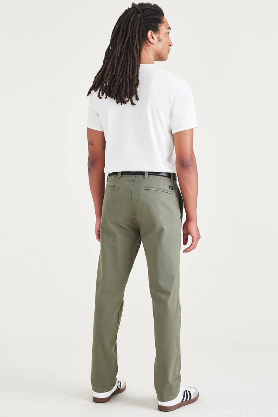 Man met dreadlocks in witte T-shirt en kaki broek.