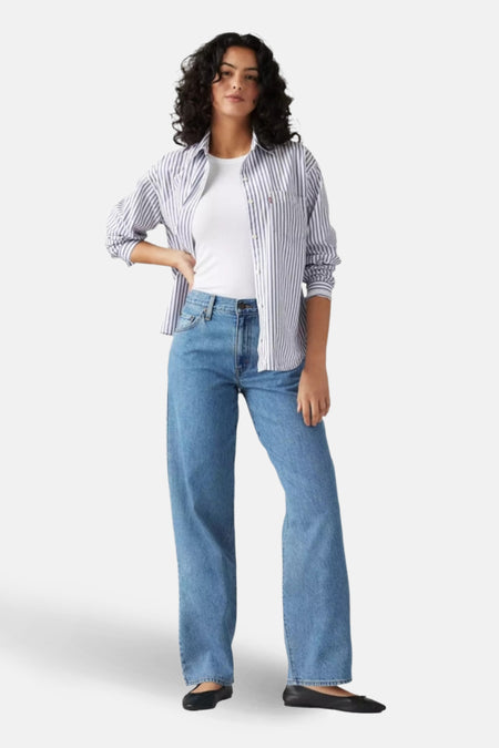 Vrouw in witte top, gestreept overhemd en blauwe jeans.