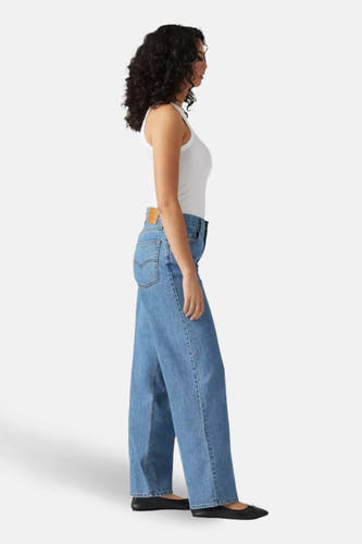 Jeans straight mid blue denim van Levi's, gedragen met een wit hemd en zwarte ballerina's, in zijaanzicht.
