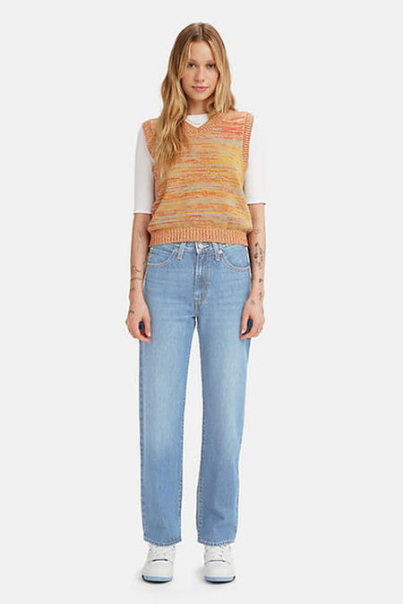 Jean droit bleu clair de Levi's, avec une ceinture haute et des poches arrière, associé à un haut tricoté avec des rayures oranges.