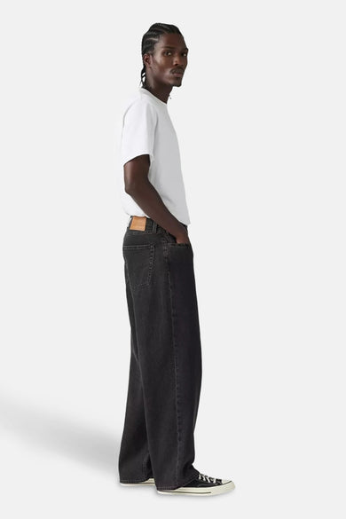 Paires de jeans gris foncé larges de Levi's, portées avec un t-shirt blanc et des baskets noires, vue latérale.