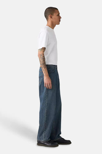 Jean droit bleu denim de Levi's®, porté avec un t-shirt blanc et des chaussures noires, vue latérale.